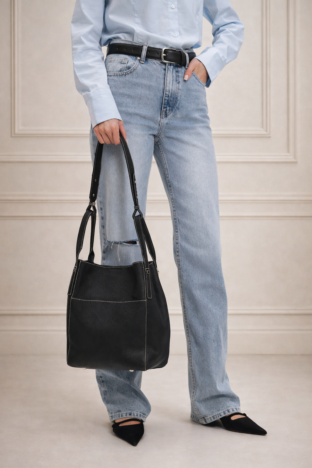 Black leather hobo bag with white stitching, carried by woman in jeans and blue shirt